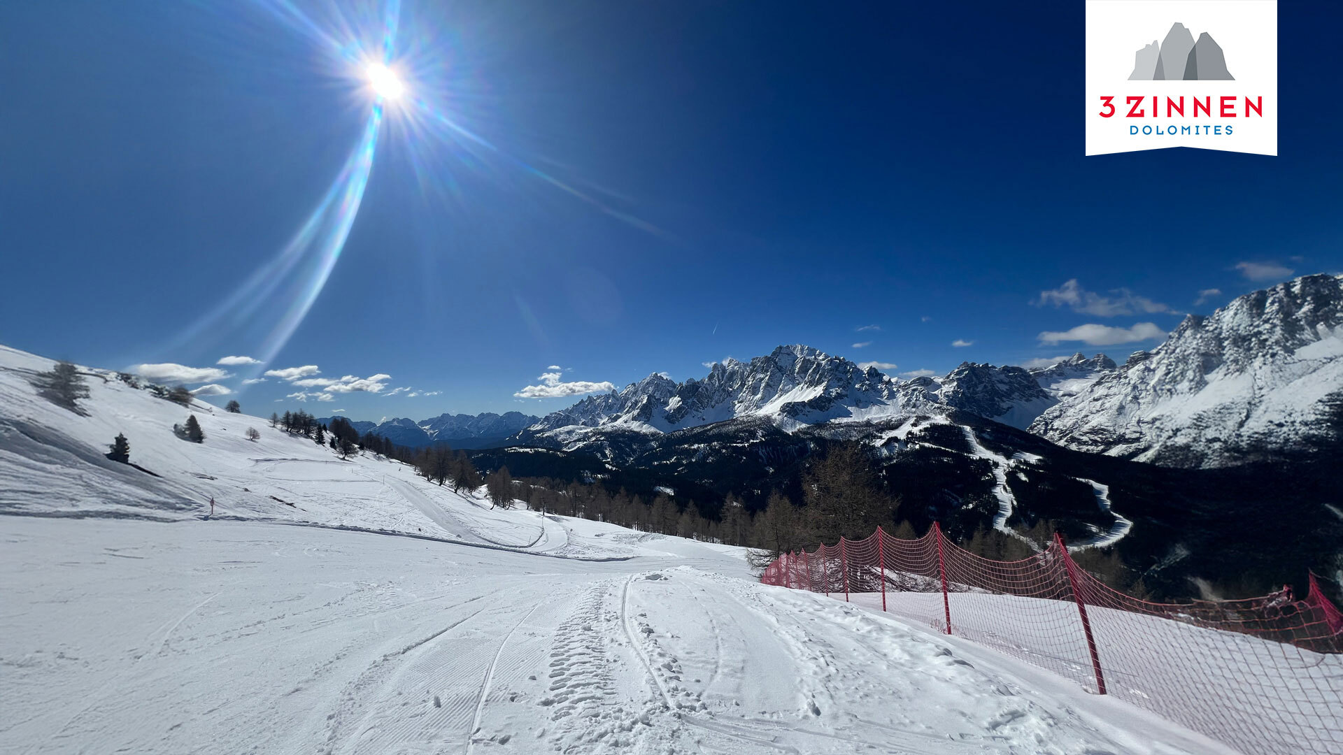 Skipiste bei Sonnenschein mit den 3Zinnen im Hintergrund und dem Logo der 3Zinnen Dolomiten